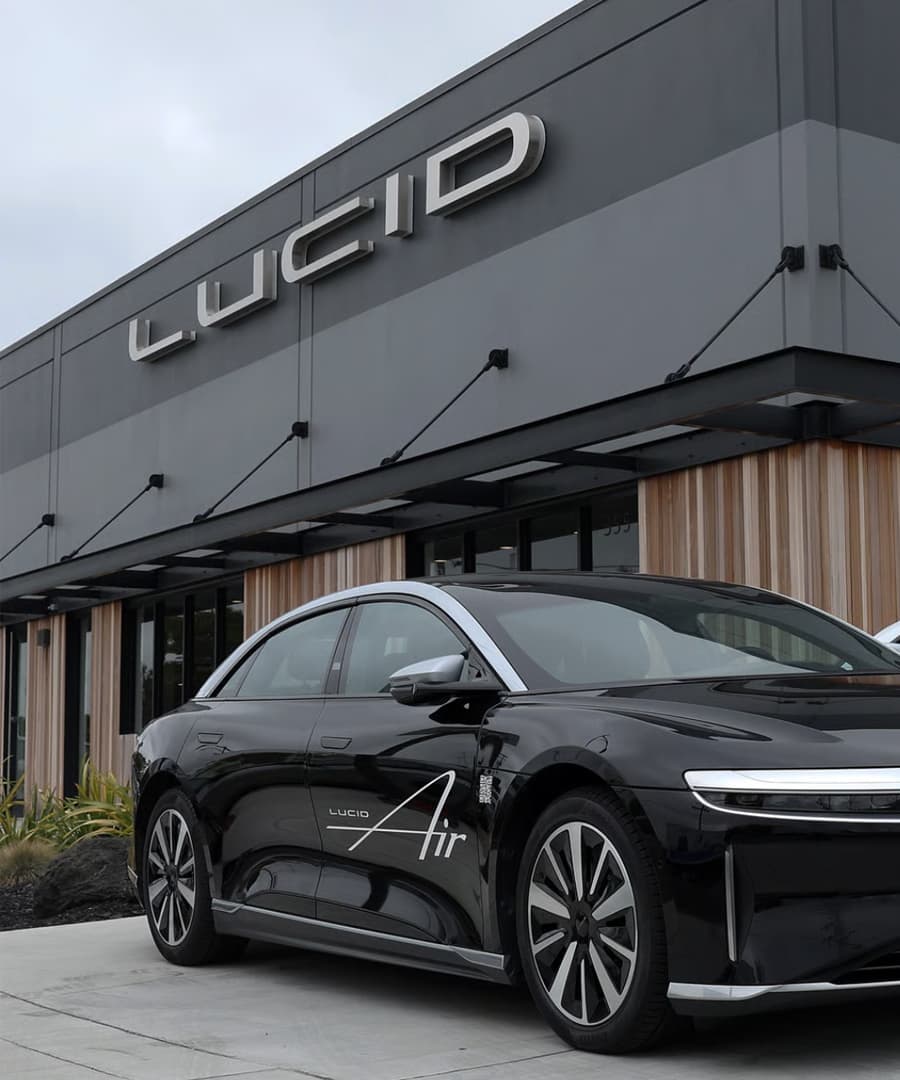 Sedán Lucid Air negro estacionado frente a un edificio con el logo de Lucid en la fachada