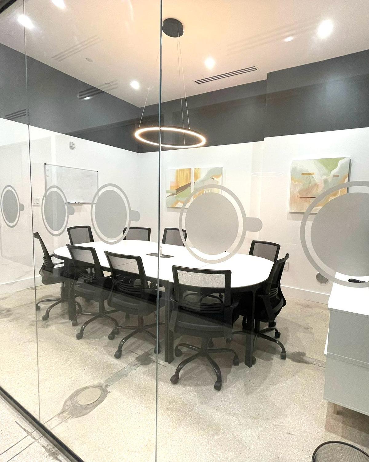 GROU Coffee + Cowork meeting room behind glass walls with coffee cup decals, a long white table and black office chairs