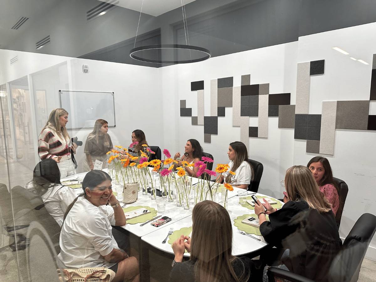 Group of women gathered around a long table decorated with pink and orange gerbera daisies in a meeting room at GROU