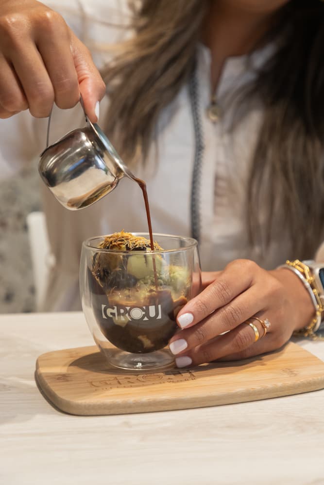 Espresso vertido desde una jarrita sobre gelato de pistacho, chocolate y kataifi crujiente en un vaso GROU