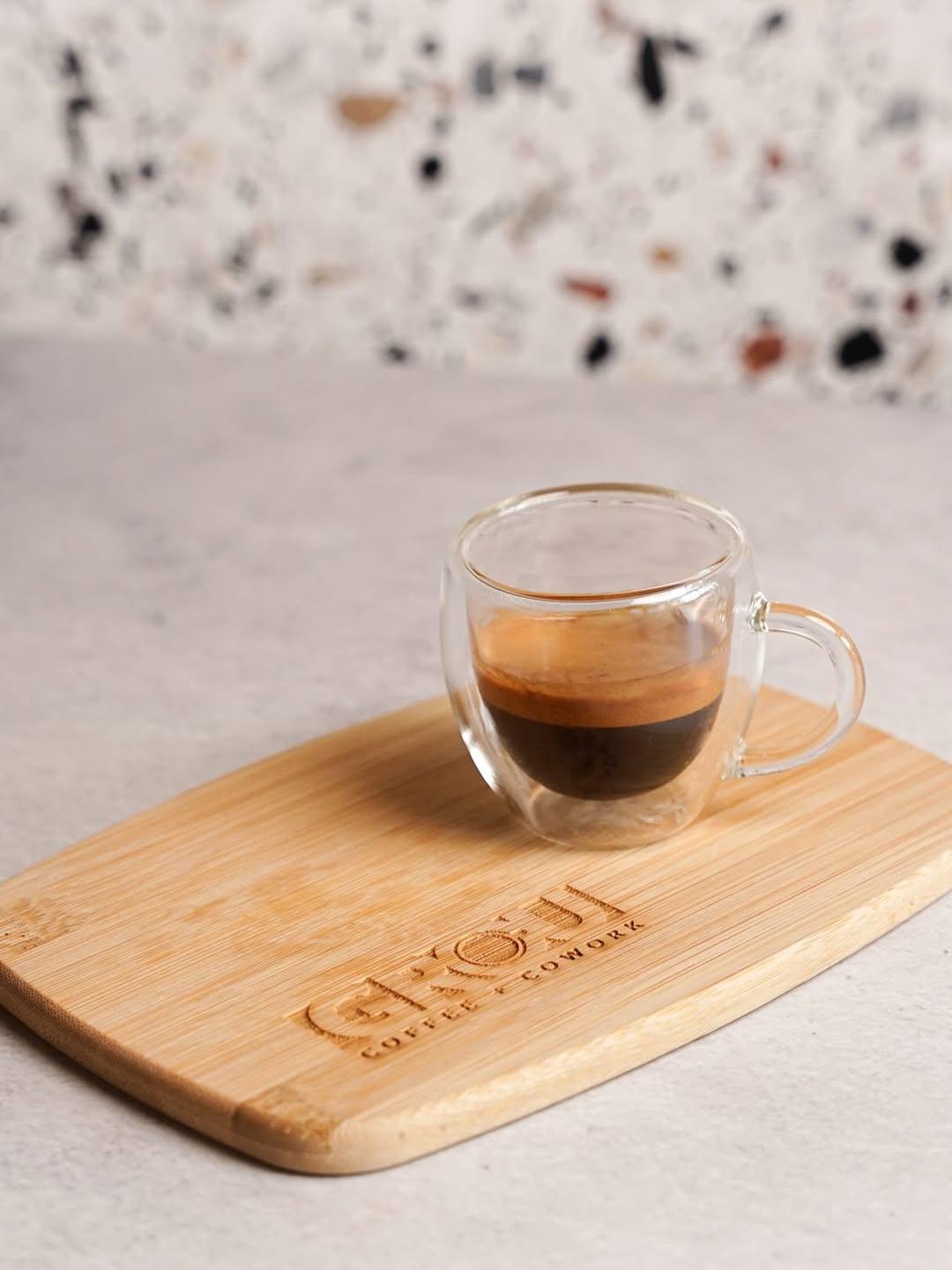 Espresso with crema in a small glass cup on a wooden board engraved with the GROU Coffee + Cowork logo
