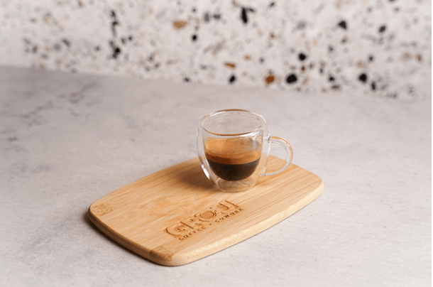 Espresso with a visible layer of crema in a small glass cup on a wooden board engraved with the GROU logo