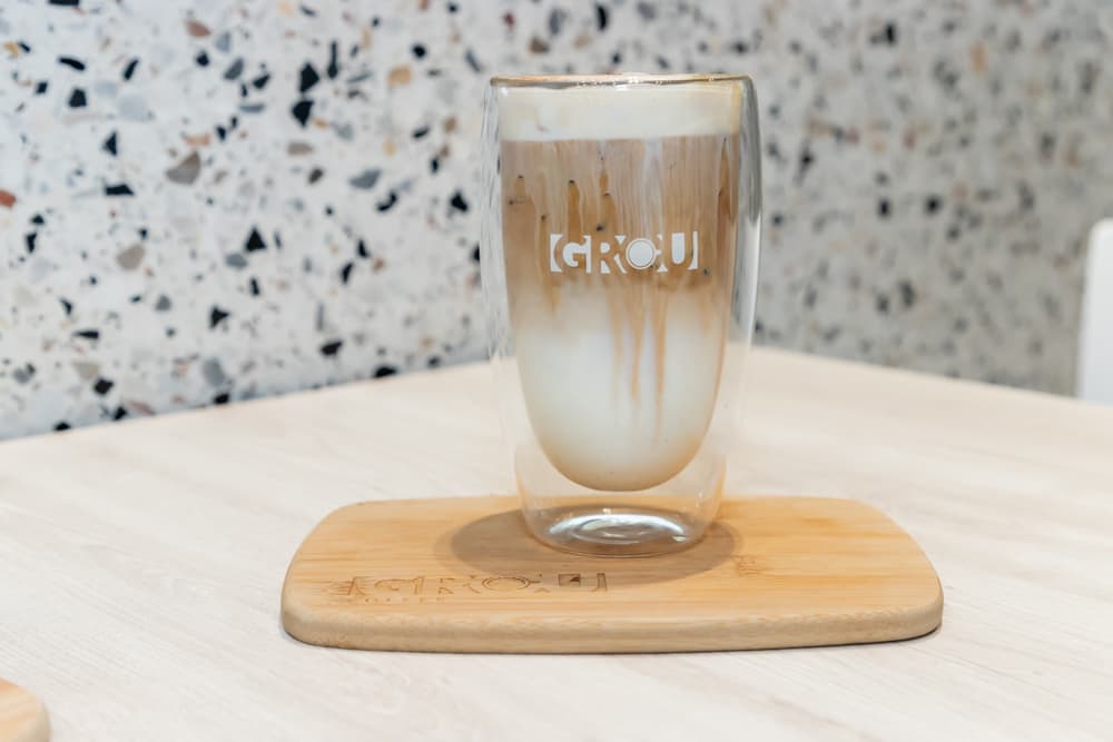 Pumpkin Spice Latte en un vaso alto de GROU, con el espresso bajando entre la leche, sobre una tabla de madera