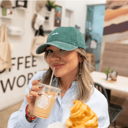 Mujer con la gorra Matcha verde en GROU, tomando una bebida y sosteniendo un croissant