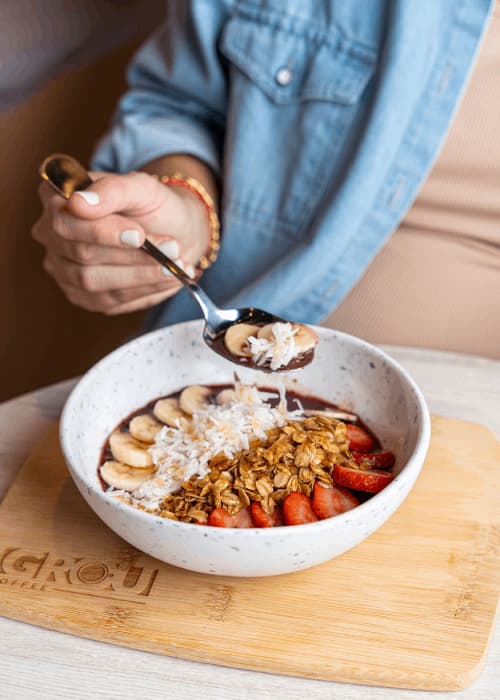 Açaí bowl con banana, fresas, granola y coco en hojuelas sobre una tabla de madera de GROU Coffee