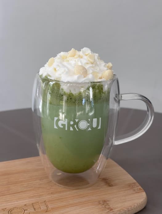 Peppermint Mocha Matcha in a GROU glass mug, topped with whipped cream and white chocolate pieces, on a wooden board